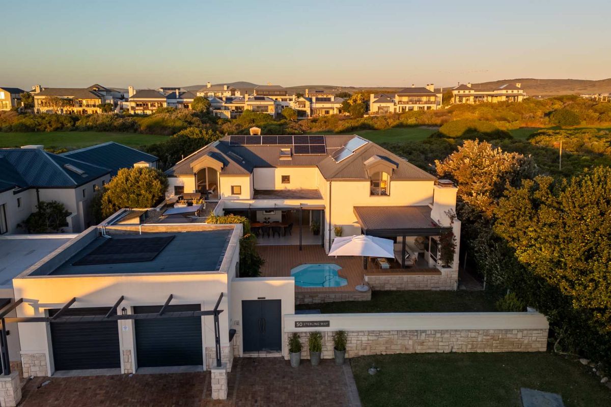 Aerial view of a modern residential property featuring a swimming pool, covered patio, solar panels, and a double garage in a landscaped estate setting.