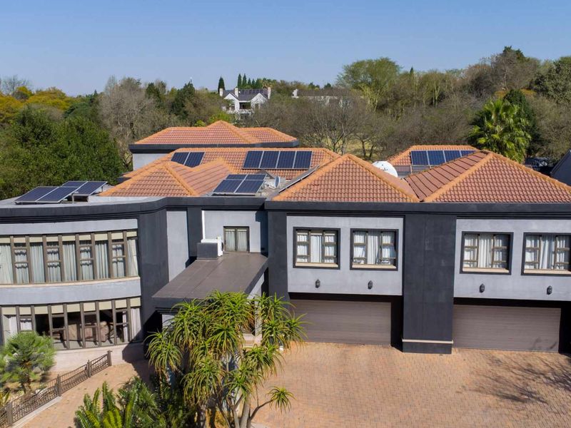 Aerial view of a modern double-story residence featuring a tiled roof with integrated solar panels, a paved driveway, and double garage access.