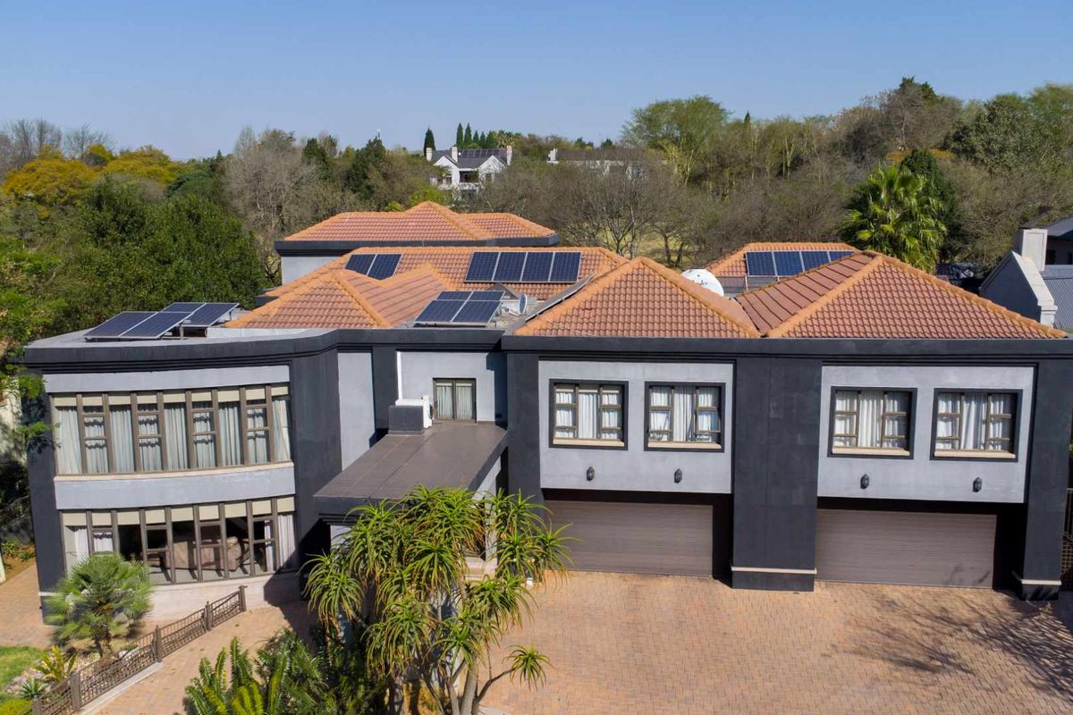 Aerial view of a modern double-story residence featuring a tiled roof with integrated solar panels, a paved driveway, and double garage access.