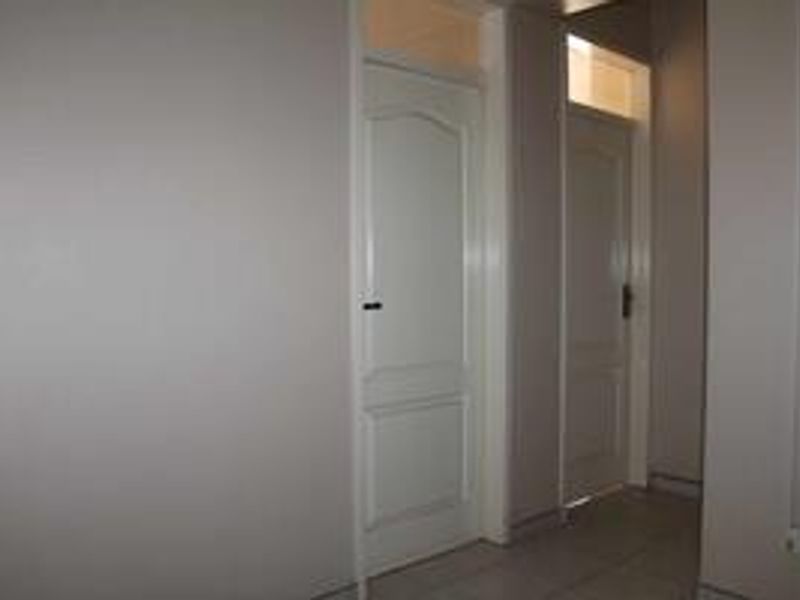 A simple, neutral hallway featuring tiled flooring and two panelled interior doors with transom windows above.