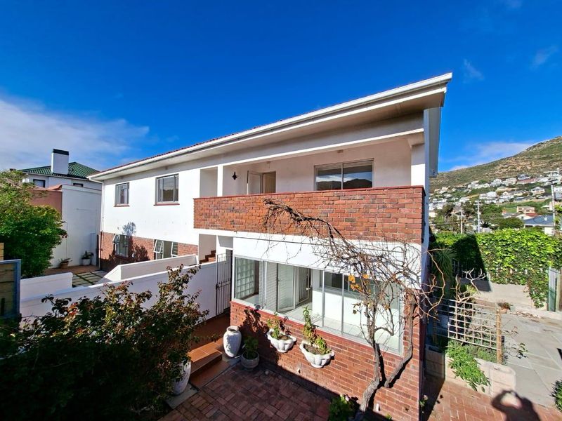 Rear view of a multi-level apartment building featuring a brick and white facade, a balcony, and a paved ground-level courtyard area.
