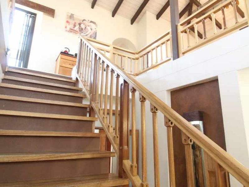A spacious hallway featuring a timber staircase with wooden balustrades, leading to an upper level with vaulted ceilings and exposed timber roof trusses.