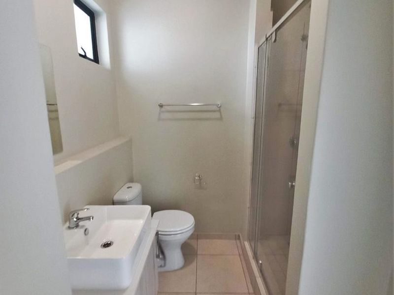 A clean and functional bathroom featuring a modern vanity, a glass-enclosed shower, and neutral floor tiling.