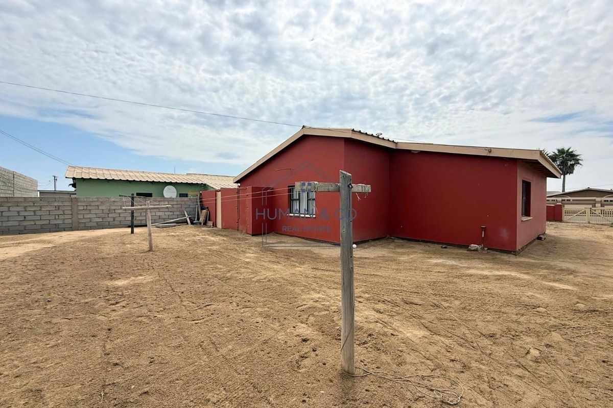 Rear view of the property featuring a large, unpaved sandy yard, perimeter boundary wall, and exterior access to the main dwelling.