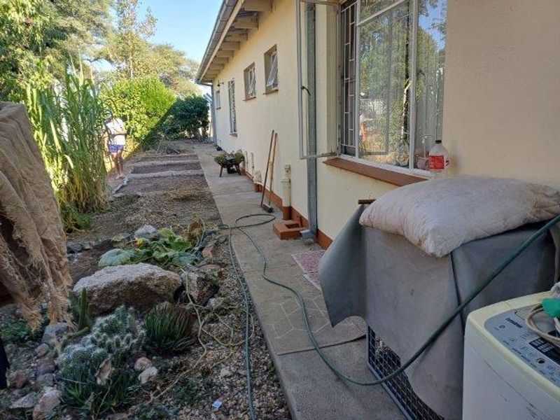 A view of the rear exterior of the house featuring a concrete pathway, garden beds, and security bars on the windows.