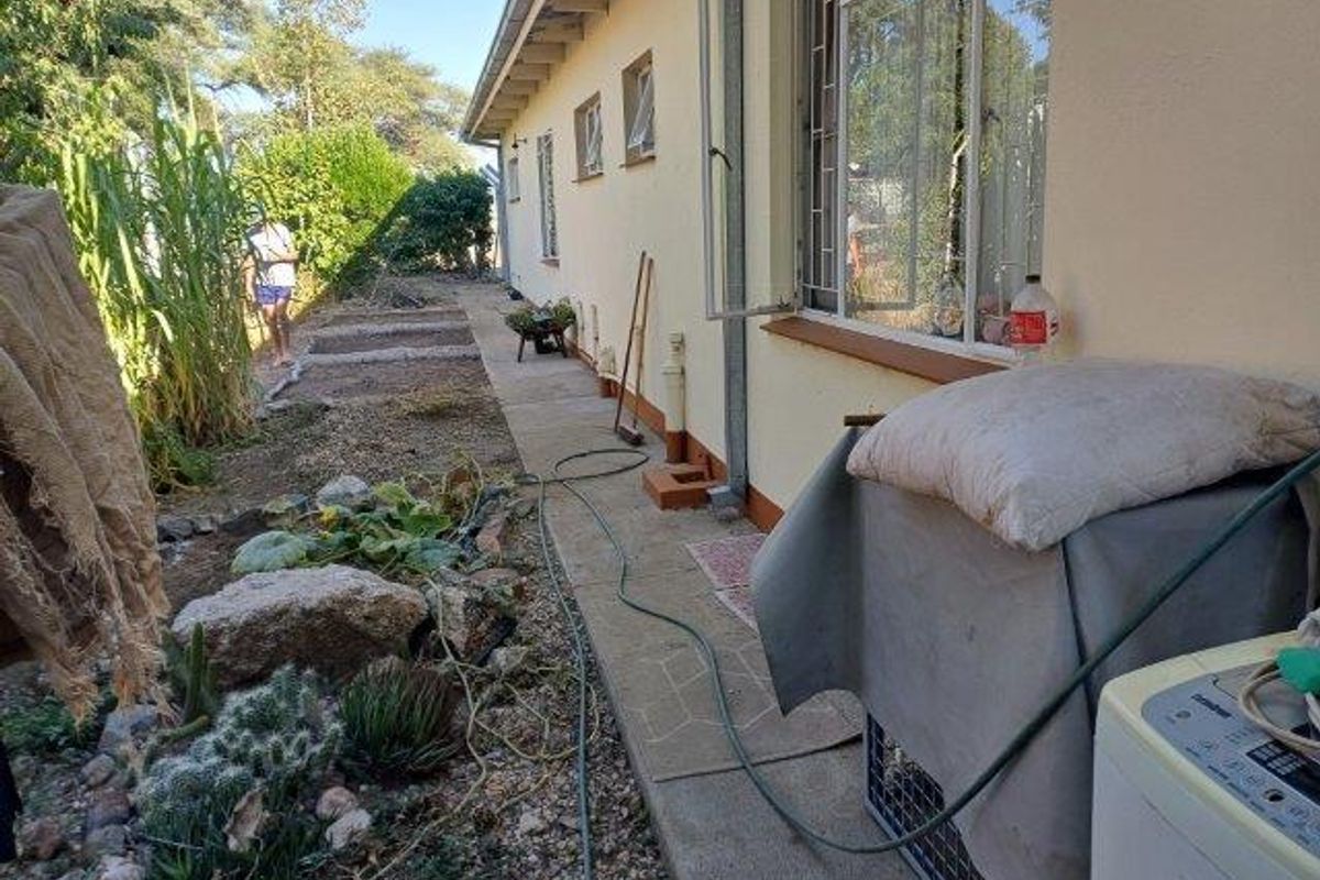 A view of the rear exterior of the house featuring a concrete pathway, garden beds, and security bars on the windows.
