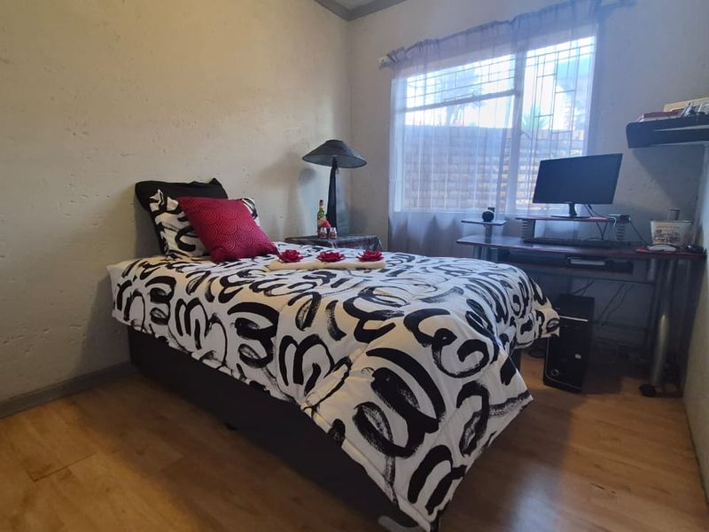 A compact bedroom featuring laminate flooring and a window fitted with security bars, providing a functional space for rest or study.