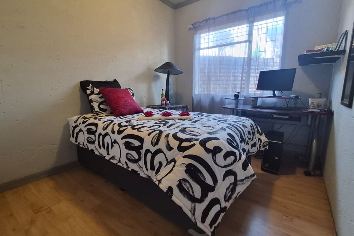 A compact bedroom featuring laminate flooring and a window fitted with security bars, providing a functional space for rest or study.