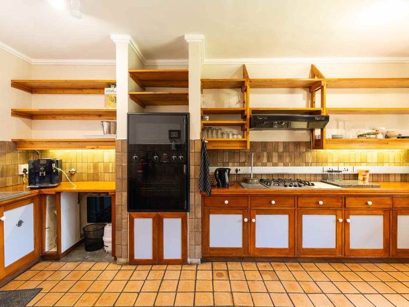 A functional kitchen featuring wooden cabinetry, open shelving, a built-in oven, gas hob, and terracotta floor tiles with a tiled backsplash.