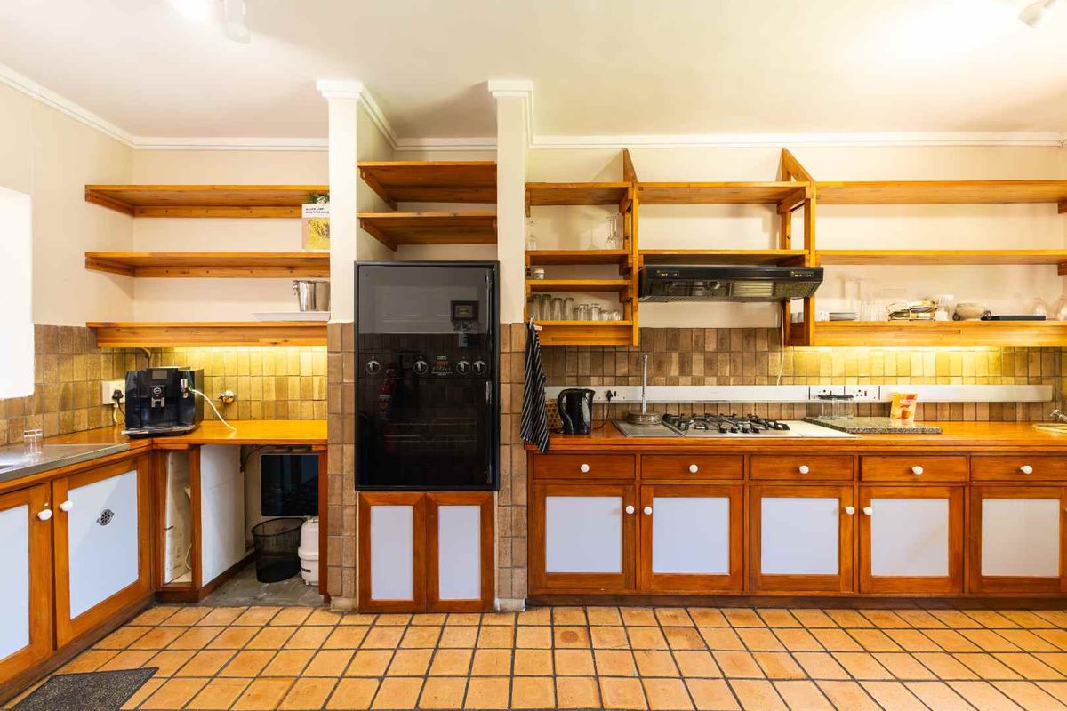 A functional kitchen featuring wooden cabinetry, open shelving, a built-in oven, gas hob, and terracotta floor tiles with a tiled backsplash.