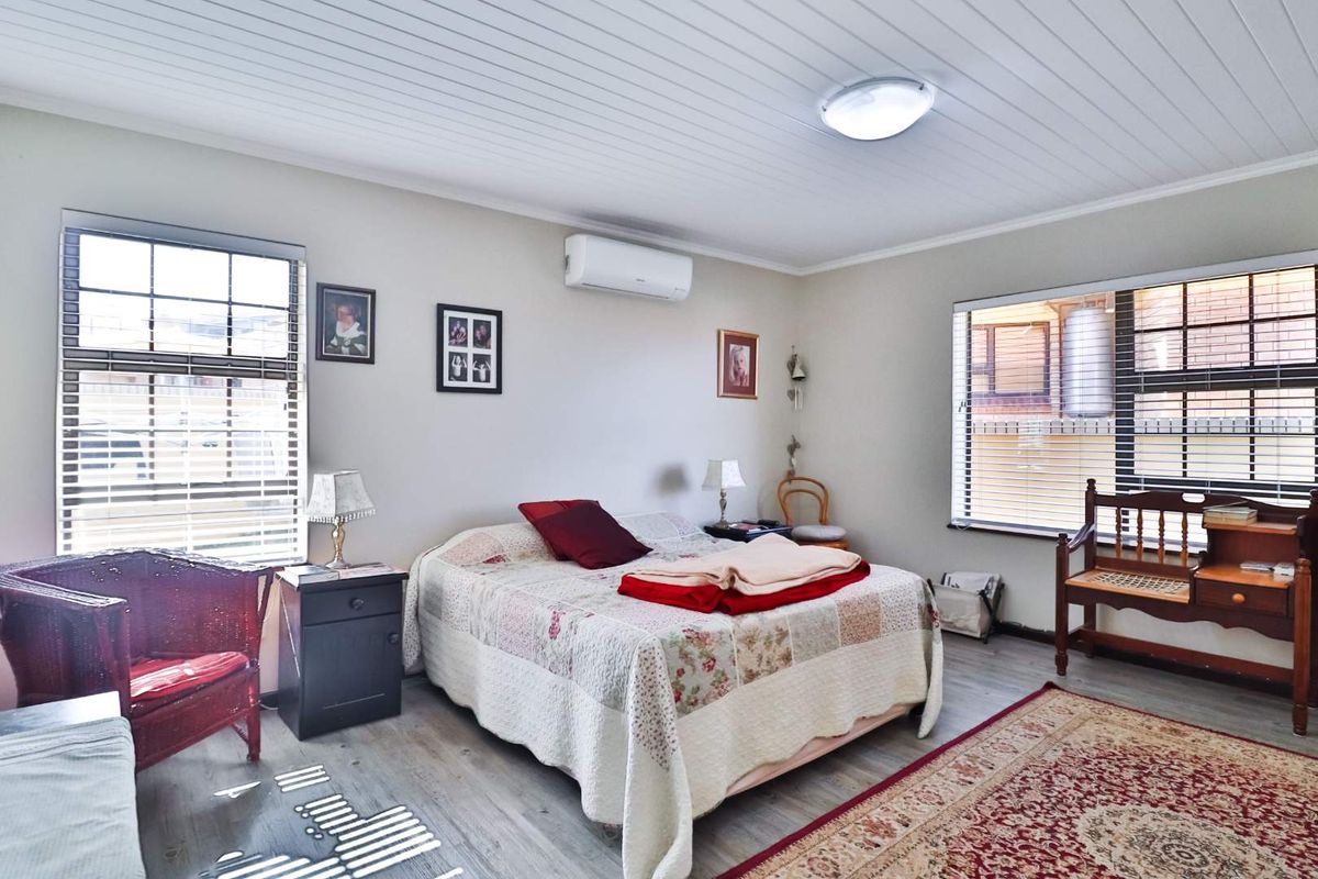 A well-lit bedroom featuring timber-look laminate flooring, a split-system air conditioner, and a tongue and groove ceiling with dual aspect windows.