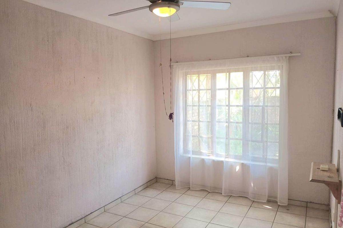 An empty bedroom featuring tiled flooring, a ceiling fan, and a window with security bars, offering a blank canvas for personalization.