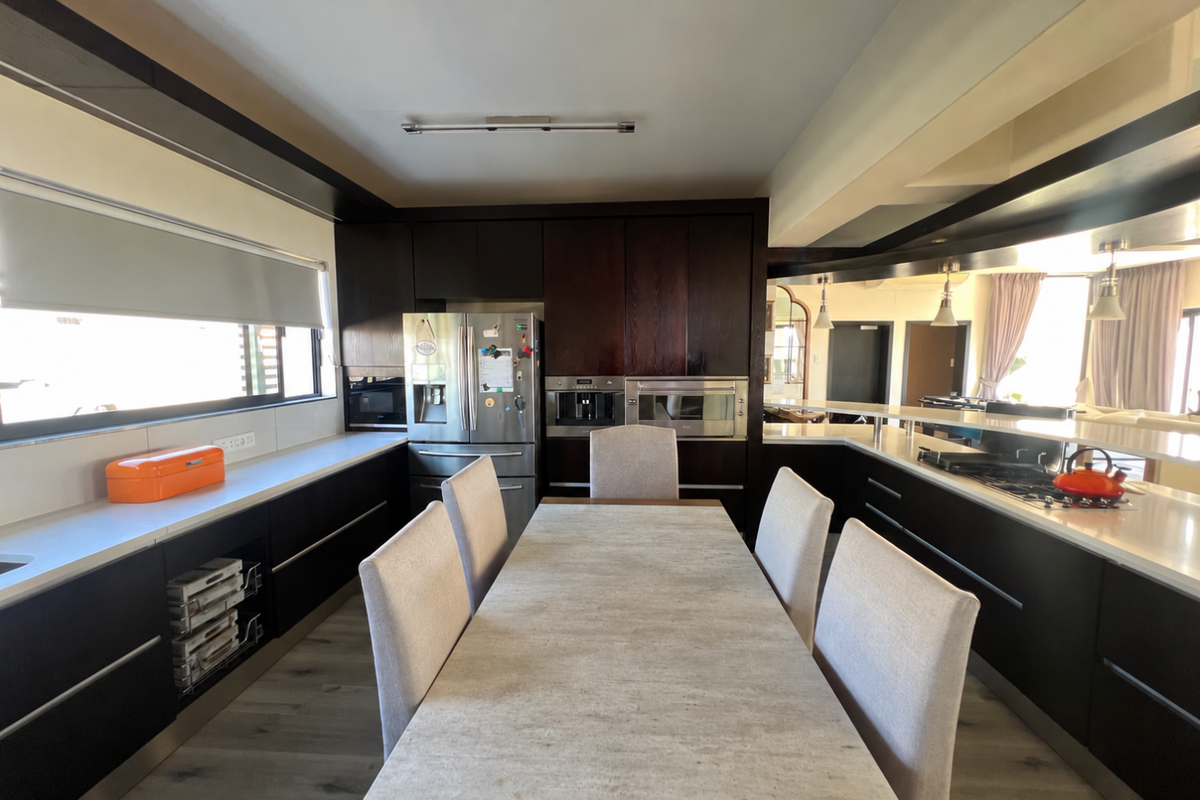Modern kitchen featuring dark wood cabinetry, stone countertops, integrated appliances, and a central dining area with a clean, contemporary aesthetic.