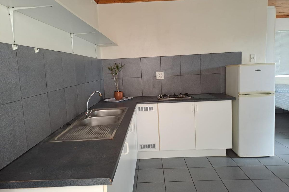 A functional kitchen featuring white cabinetry, dark laminate countertops, a double bowl stainless steel sink, built-in gas hob, and grey tiled splashback.
