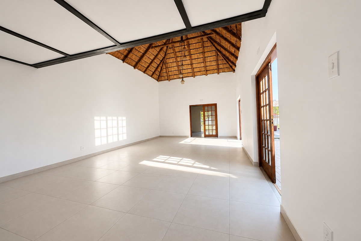 Spacious, light-filled living area featuring a high thatched ceiling with exposed beams, neutral tiled flooring, and direct access to the outdoor area via french doors.