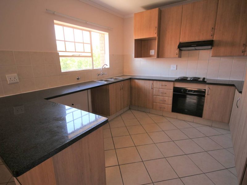 A clean, functional kitchen featuring laminate cabinetry, granite countertops, built-in oven, electric hob, and tiled flooring.
