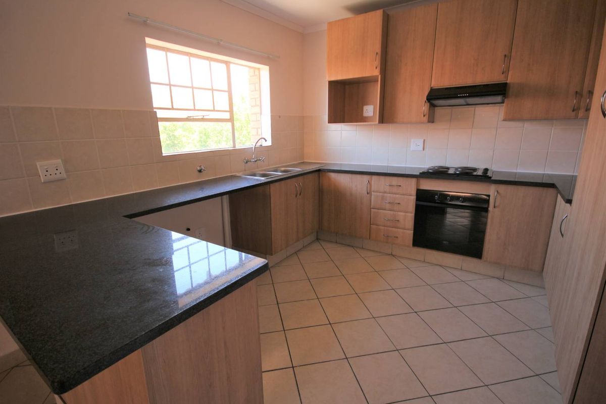A clean, functional kitchen featuring laminate cabinetry, granite countertops, built-in oven, electric hob, and tiled flooring.