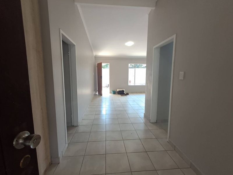 A bright, empty hallway featuring neutral tiled flooring and clean wall finishes, leading towards an open living area with natural light.