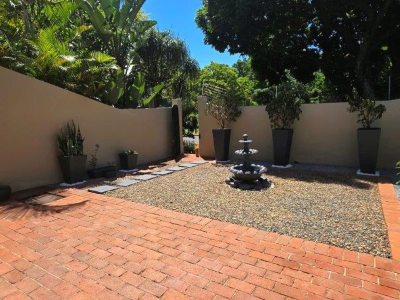 A well-maintained rear courtyard featuring brick paving, a gravel garden area, and a central stone water feature enclosed by a boundary wall.