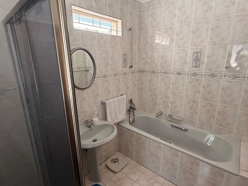 A functional bathroom featuring a built-in bathtub, separate shower enclosure, and pedestal basin with neutral ceramic wall and floor tiling.