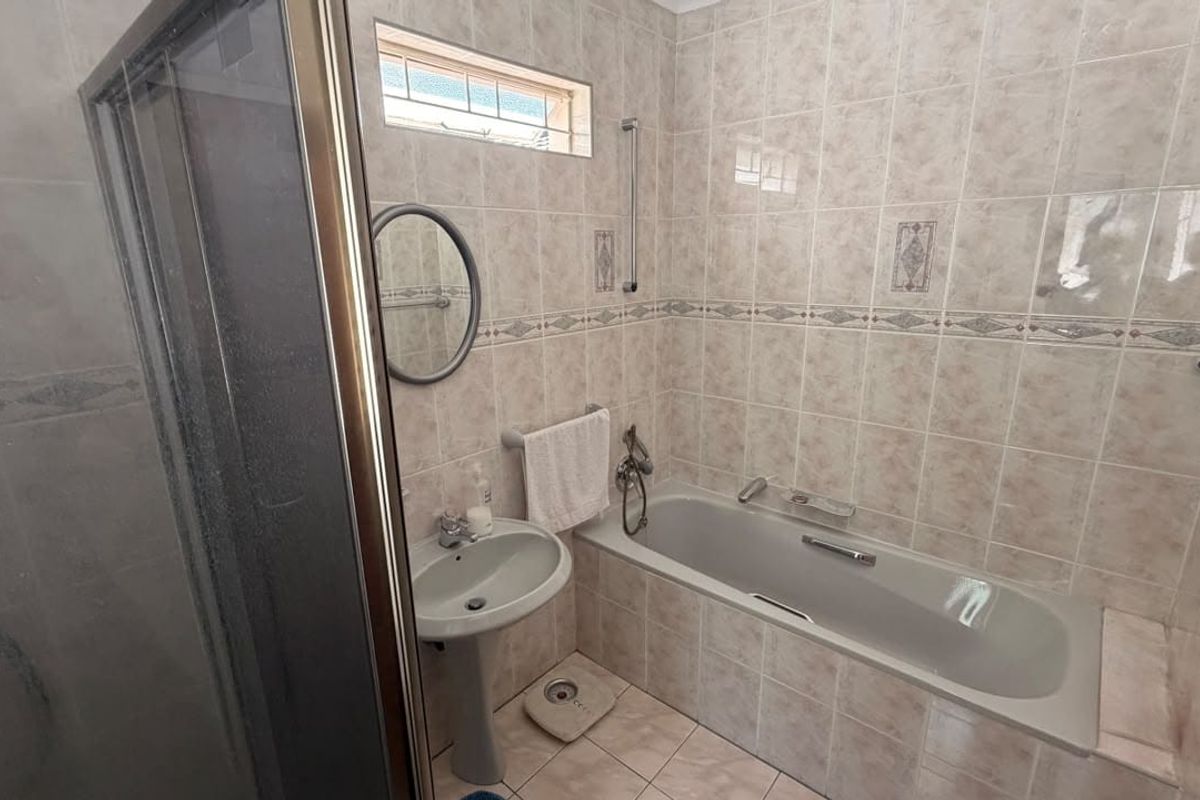 A functional bathroom featuring a built-in bathtub, separate shower enclosure, and pedestal basin with neutral ceramic wall and floor tiling.