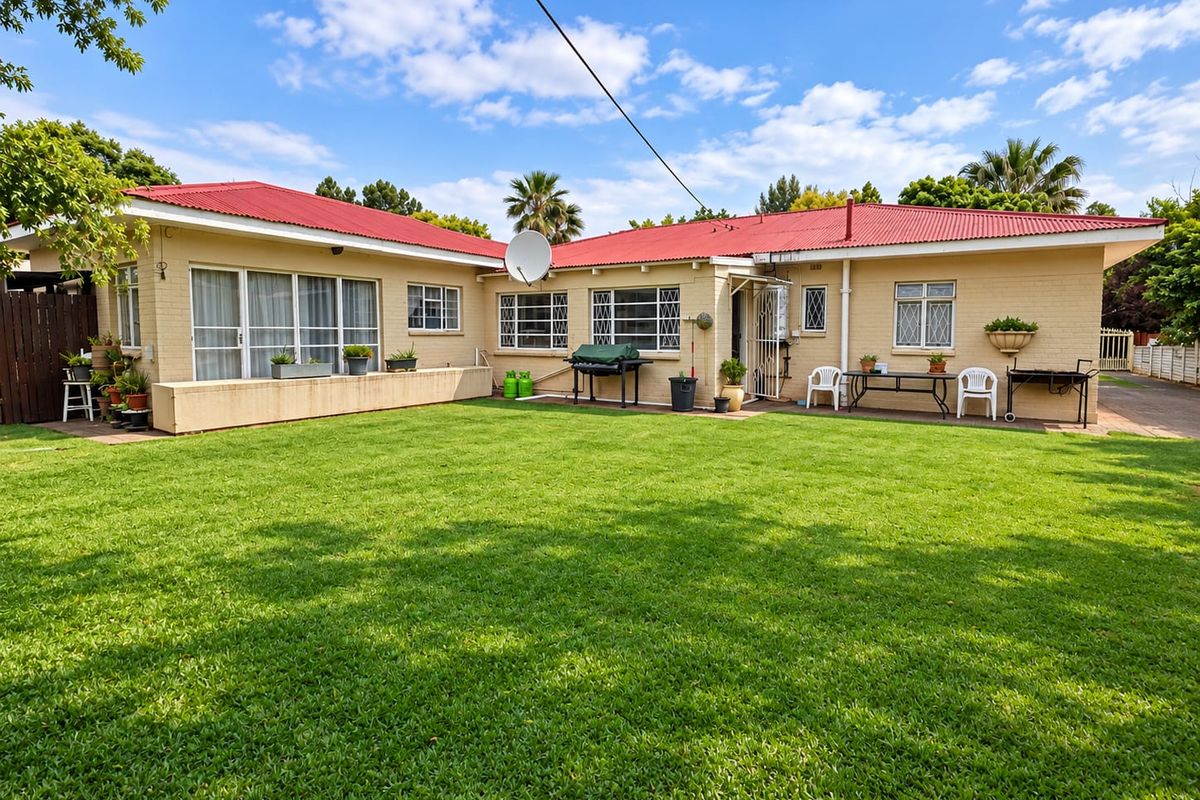 Rear view of the house featuring a well-maintained lawn, paved patio area, and a red corrugated metal roof.