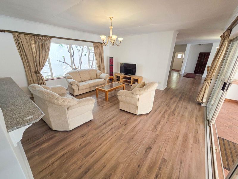 Spacious living room featuring modern laminate flooring, a large window, and direct access to an outdoor patio area through sliding glass doors.