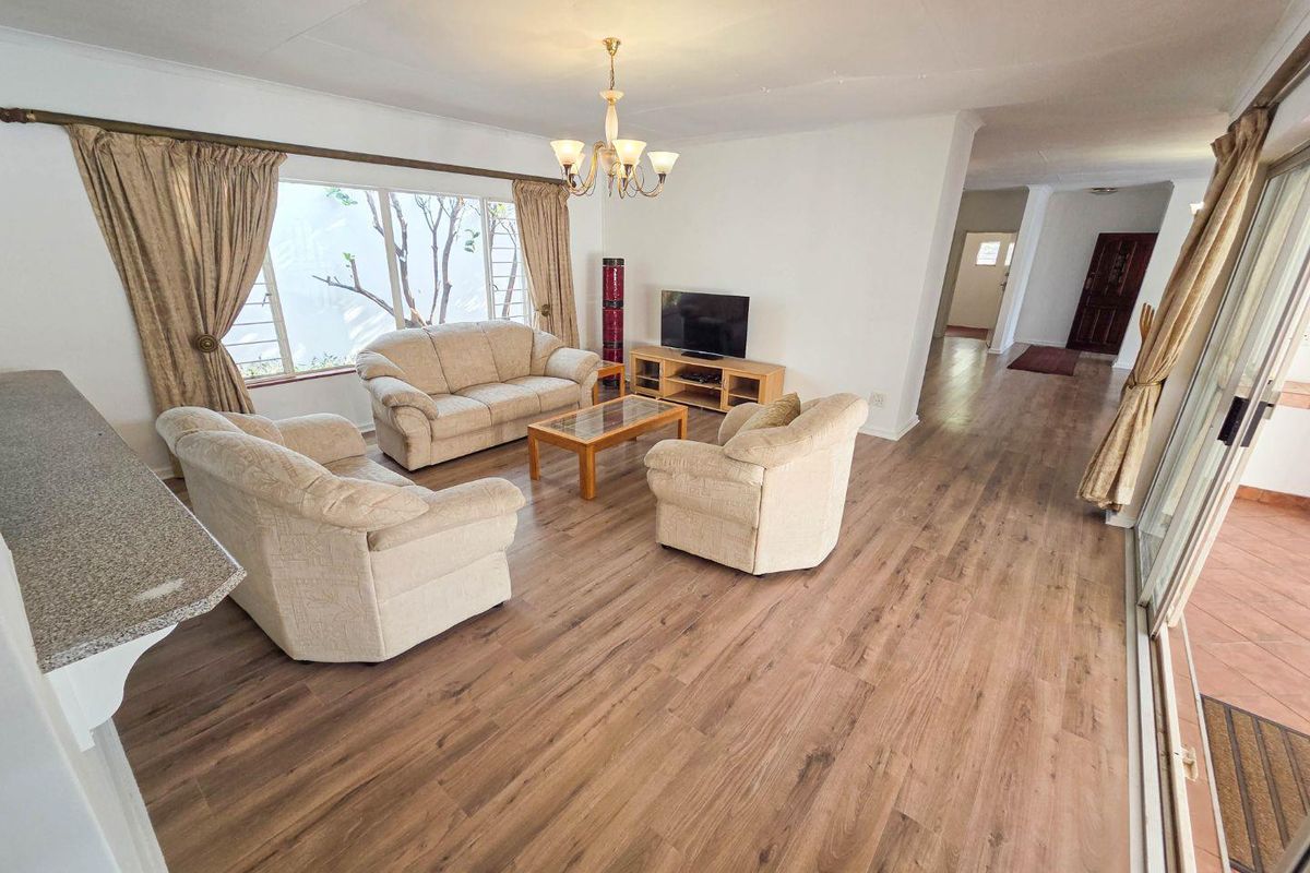 Spacious living room featuring modern laminate flooring, a large window, and direct access to an outdoor patio area through sliding glass doors.