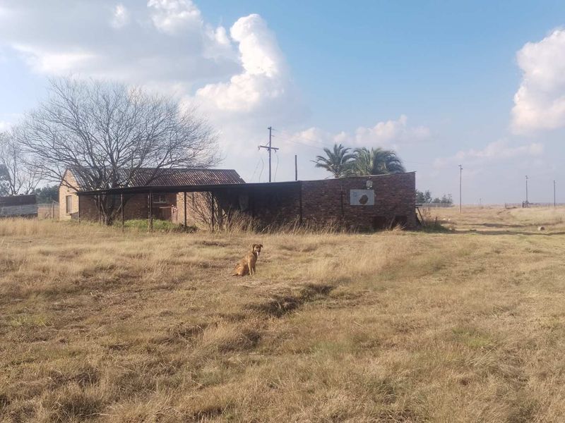 A view of the rear exterior of a farm building featuring brick construction and a covered patio area set within a rural landscape.