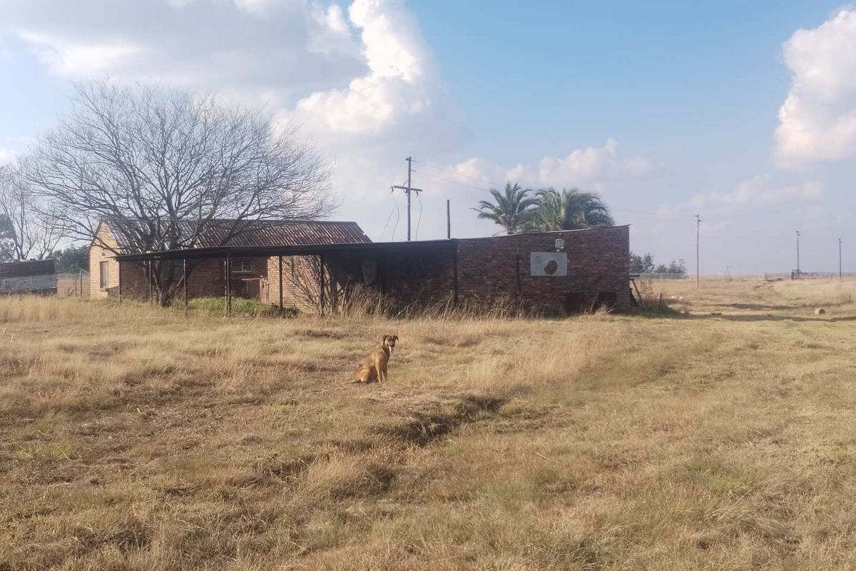 A view of the rear exterior of a farm building featuring brick construction and a covered patio area set within a rural landscape.