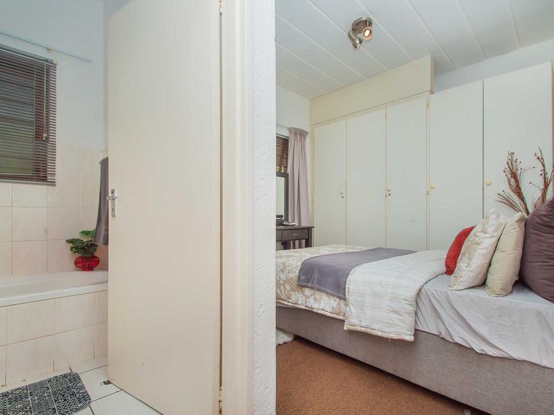 A bedroom featuring built-in cupboards and an adjacent bathroom with a tiled bathtub area.