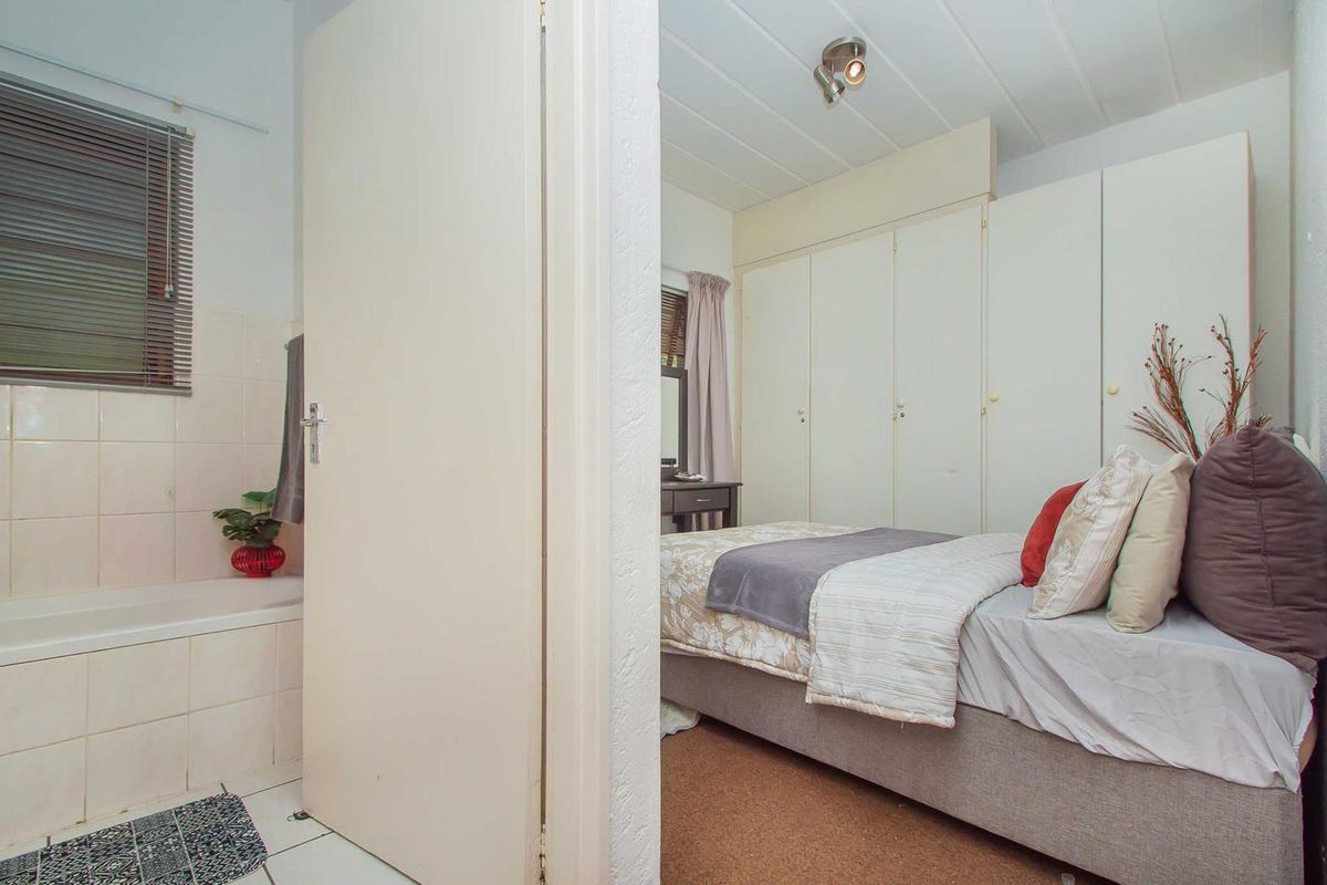 A bedroom featuring built-in cupboards and an adjacent bathroom with a tiled bathtub area.