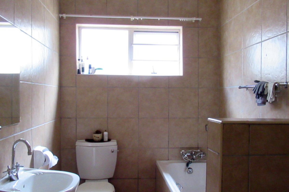 A functional bathroom featuring full-height wall tiling, a built-in bathtub, a pedestal basin, and a toilet.