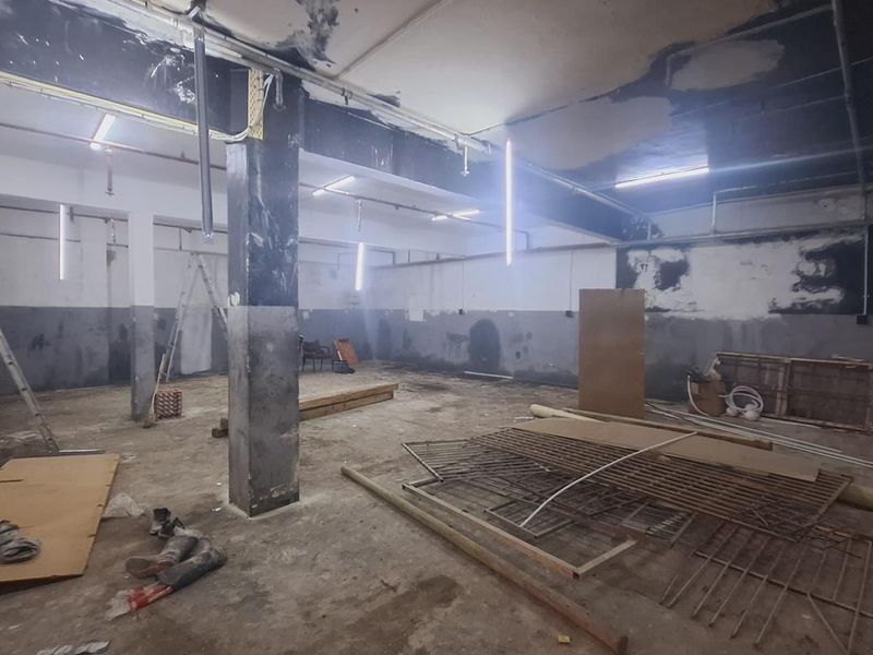 Large industrial utility space featuring exposed concrete columns, high ceilings with exposed piping, and unfinished wall surfaces, suitable for renovation or storage.