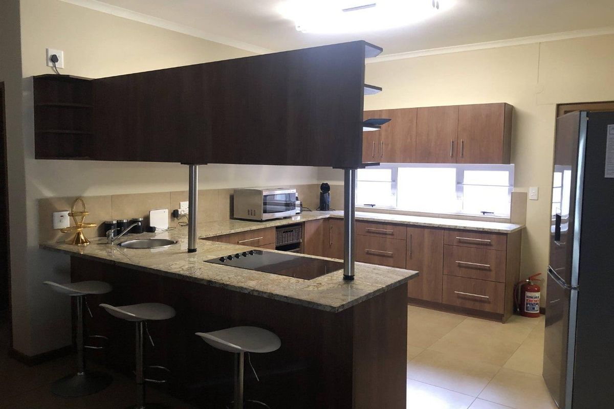 A functional kitchen featuring wood-finish cabinetry, granite countertops, a breakfast bar with integrated hob, and tiled flooring.