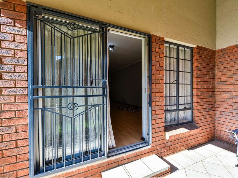 Covered patio area featuring brick exterior walls, tiled flooring, and a secure metal gate entrance leading into the interior living space.