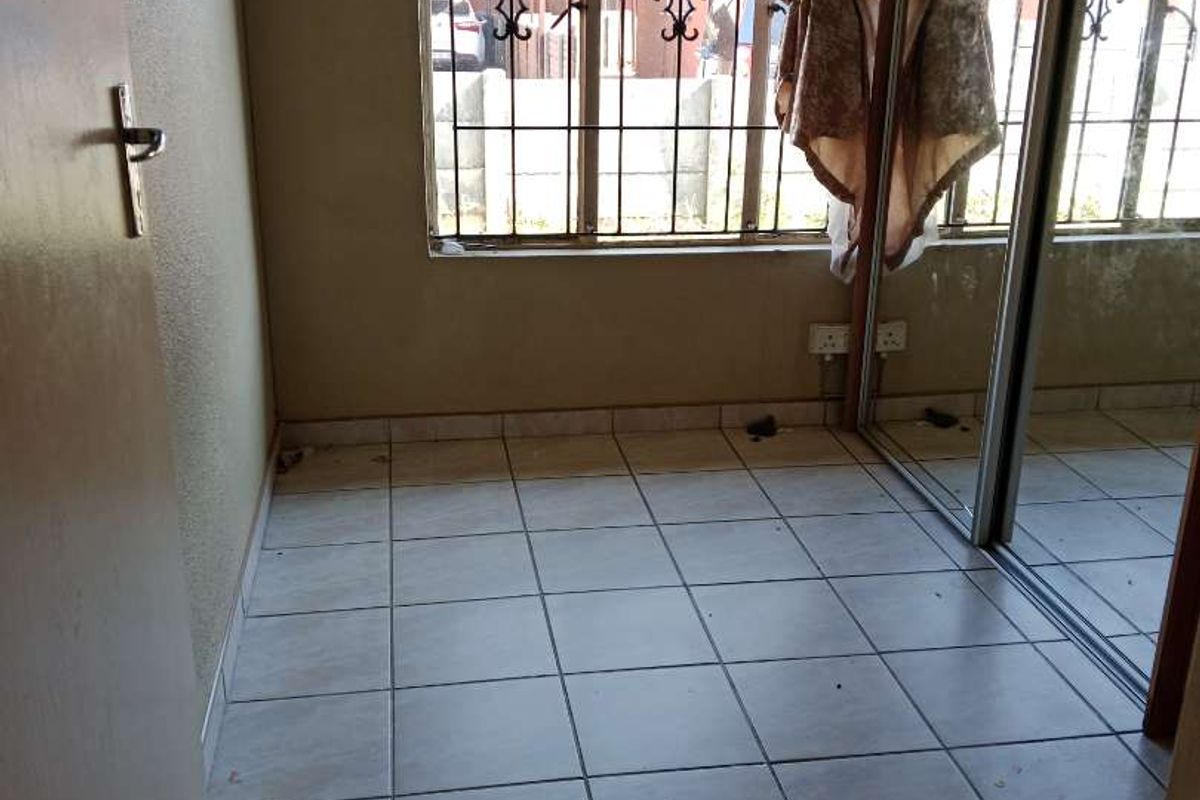 A bedroom featuring tiled flooring, built-in mirrored cupboards, and security bars on the windows.