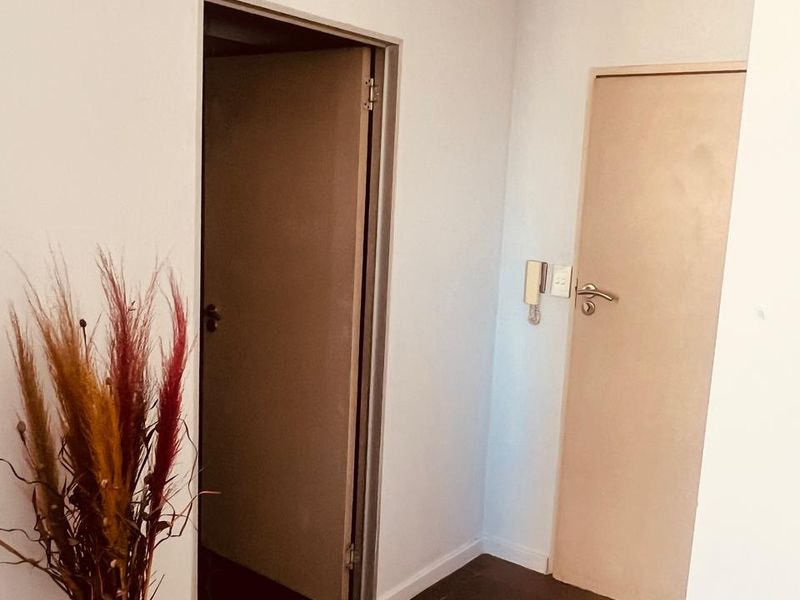 A clean and neutral hallway featuring tiled flooring and an integrated intercom system, providing access to adjacent rooms.