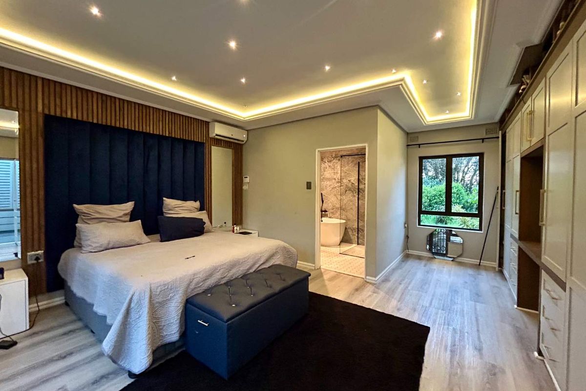 Spacious master bedroom featuring recessed tray ceiling with ambient lighting, built-in cabinetry, and an en-suite bathroom with a modern walk-in shower.