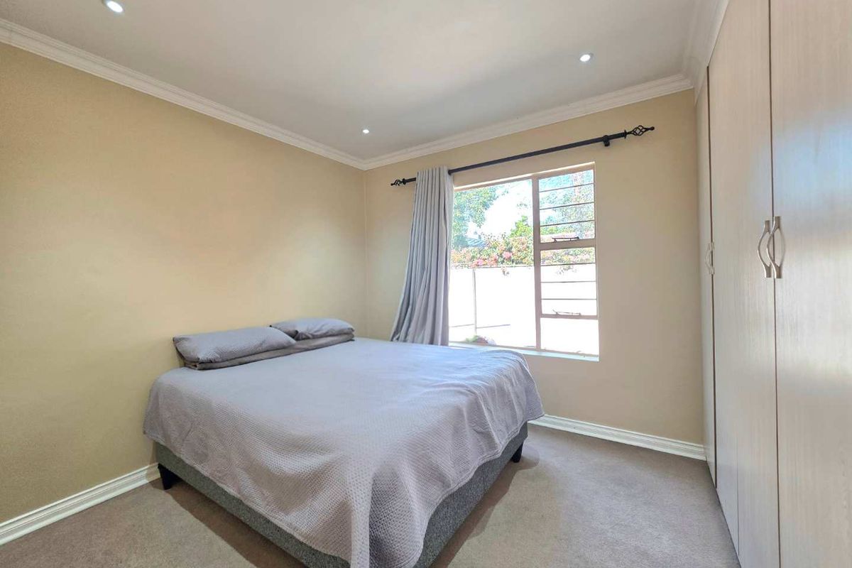 A well-lit bedroom featuring neutral wall tones, built-in cupboards, carpeted flooring, and a window with security bars.