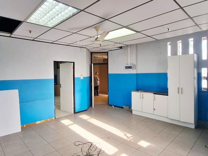An empty office space featuring tiled flooring, built-in cabinetry, and a suspended ceiling with integrated lighting, requiring cosmetic updates.