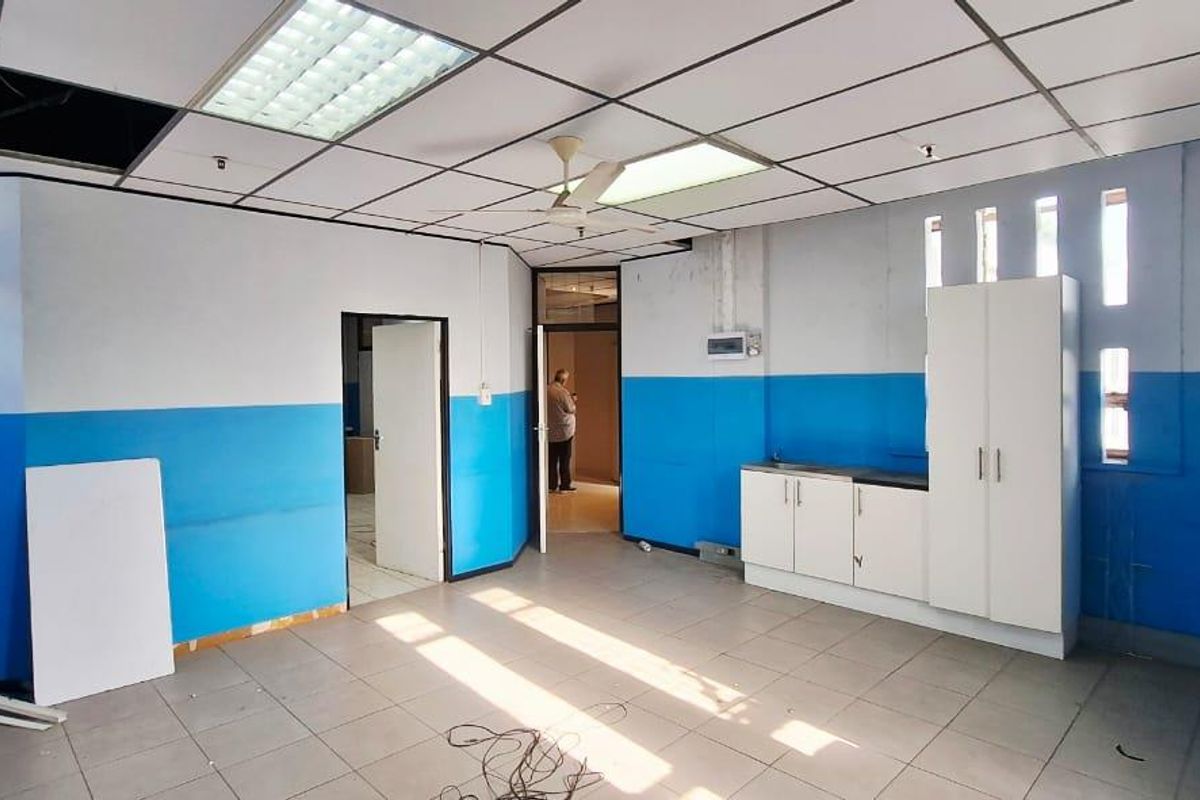 An empty office space featuring tiled flooring, built-in cabinetry, and a suspended ceiling with integrated lighting, requiring cosmetic updates.