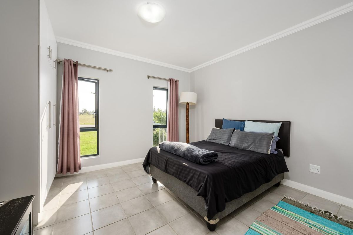 A well-maintained bedroom featuring neutral tiled flooring, built-in cupboards, and large windows that provide ample natural light.