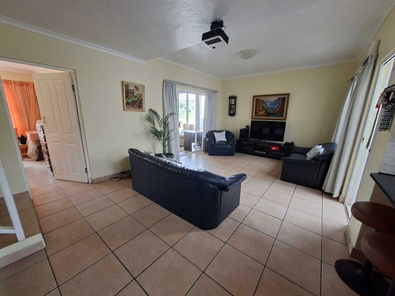 Spacious living room featuring tiled flooring, a ceiling-mounted projector, and sliding glass doors providing access to the outdoor area.