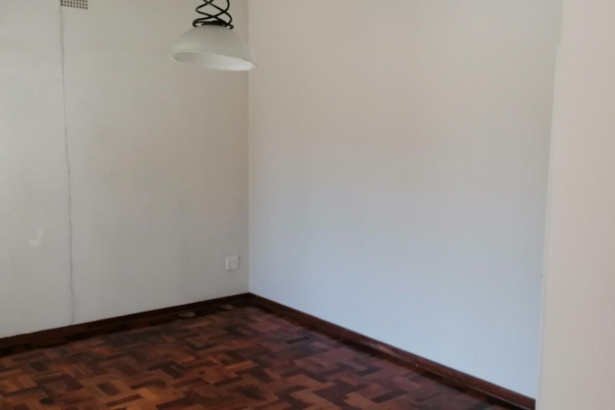 An empty bedroom featuring traditional parquet flooring, a pendant light fixture, and neutral walls with a visible crack.