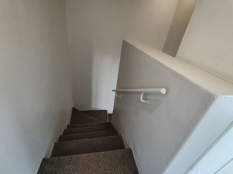 A view looking down a carpeted staircase featuring a simple white handrail and neutral wall finishes.
