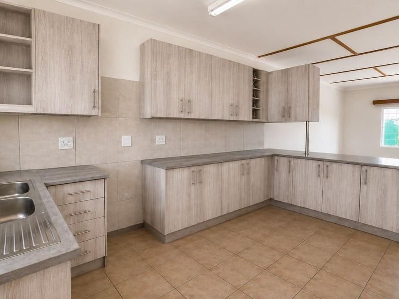 A clean, functional kitchen featuring light wood-grain cabinetry, ample laminate counter space, a double sink, and neutral tiled flooring with an integrated breakfast bar.