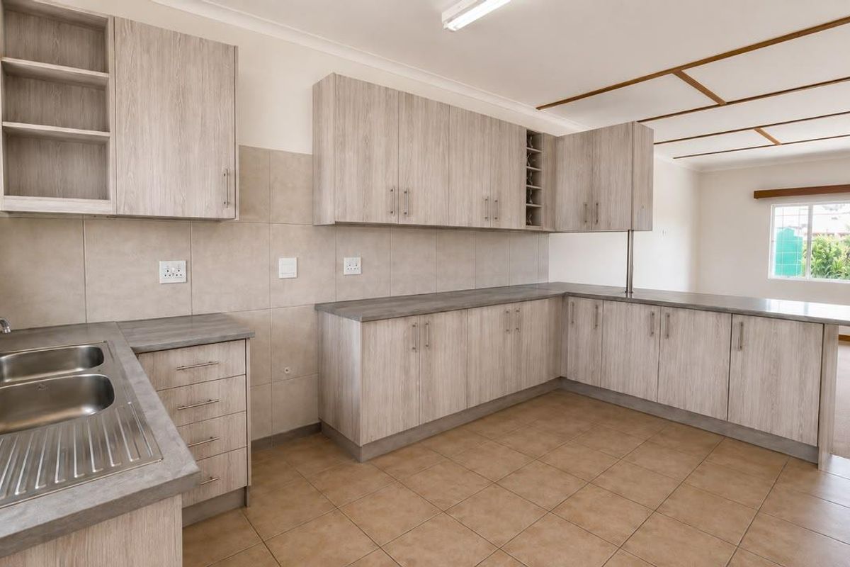 A clean, functional kitchen featuring light wood-grain cabinetry, ample laminate counter space, a double sink, and neutral tiled flooring with an integrated breakfast bar.