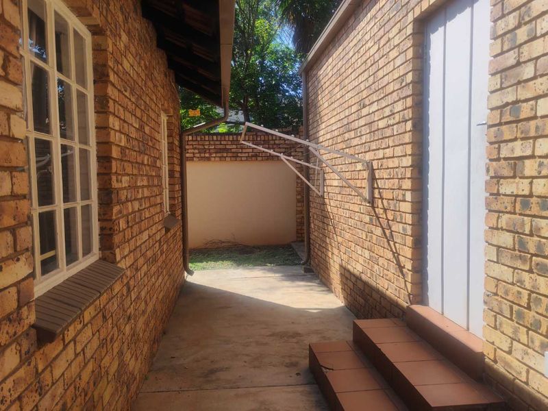 A side exterior passage featuring face brick walls, concrete paving, and a wall-mounted clothesline, leading to a small rear garden area.