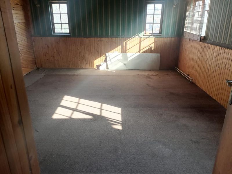 An empty bedroom featuring timber wall paneling and casement windows, requiring cosmetic updates and flooring replacement.